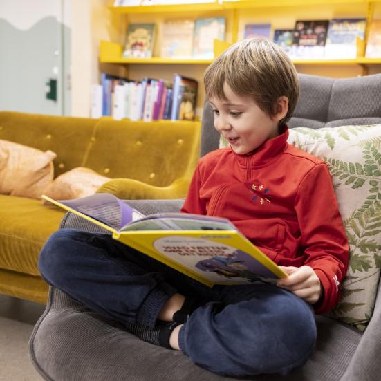 Dreng i lænestol på biblioteket der læser