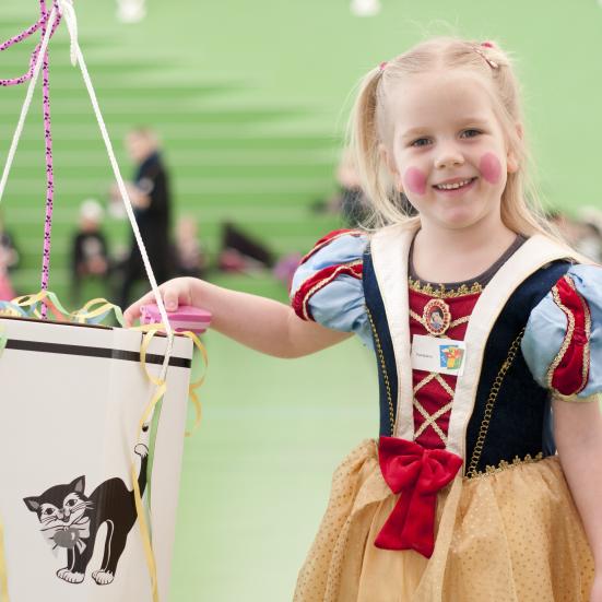 Smilende lille pige klædt ud som prinsesse ved siden af en fastelavnstønde.