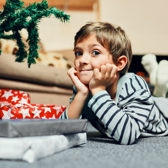 Dreng der ligger ved et juletræ med gaver og venter