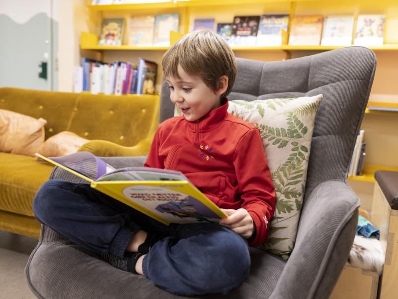 Dreng i lænestol på biblioteket der læser