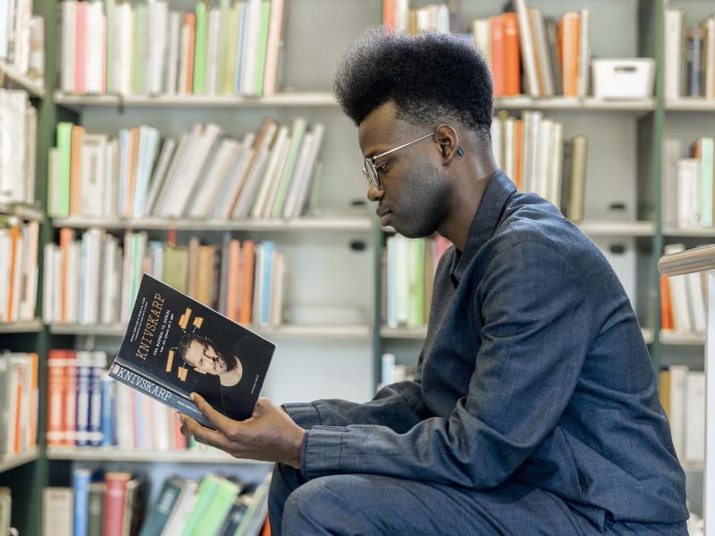 Ung mand læser en bog på biblioteket