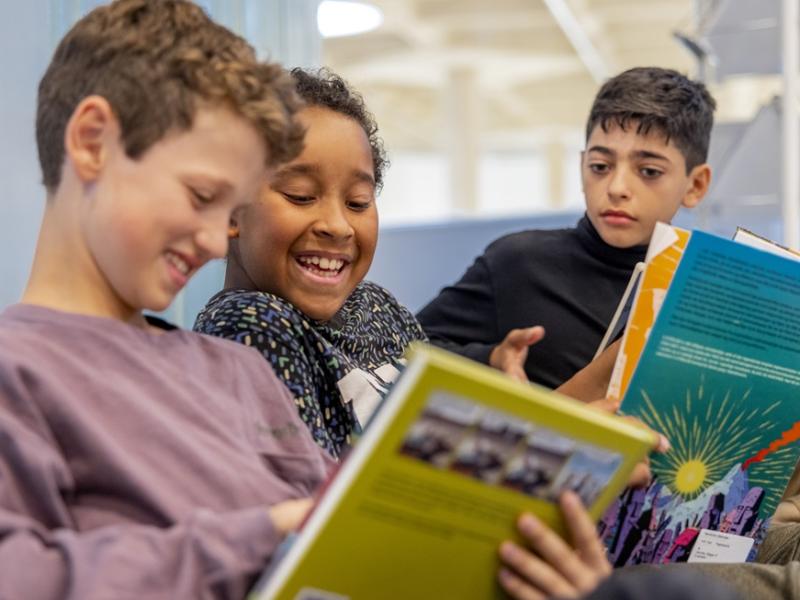 Tre smilende drenge læser i bøger på biblioteket