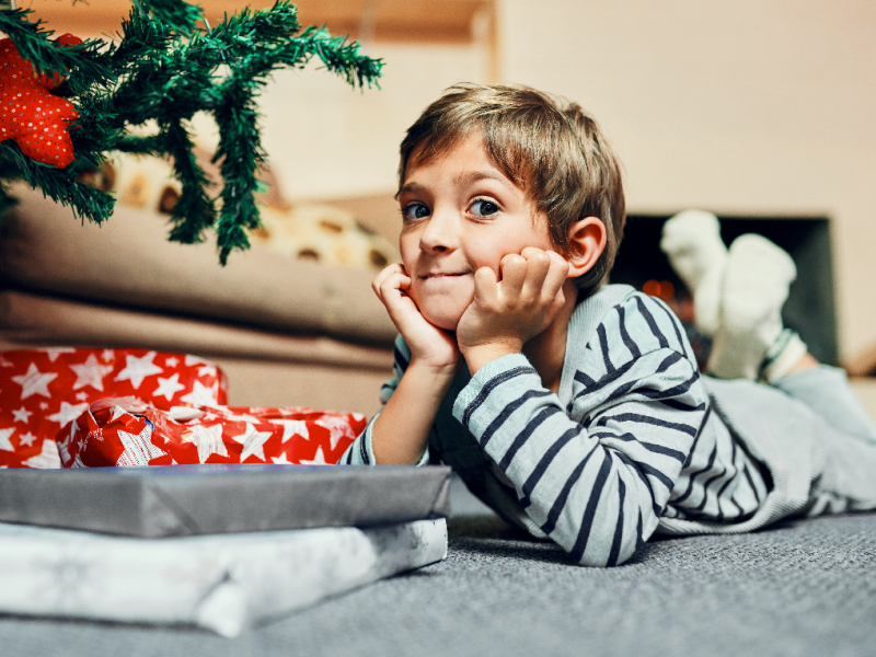 Dreng der ligger ved et juletræ med gaver og venter